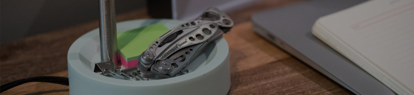 Translation missing: fr.Stainless Steel Leatherman Skeletool® resting on a desk organizer beside a notebook and sticky notes in a modern workspace.