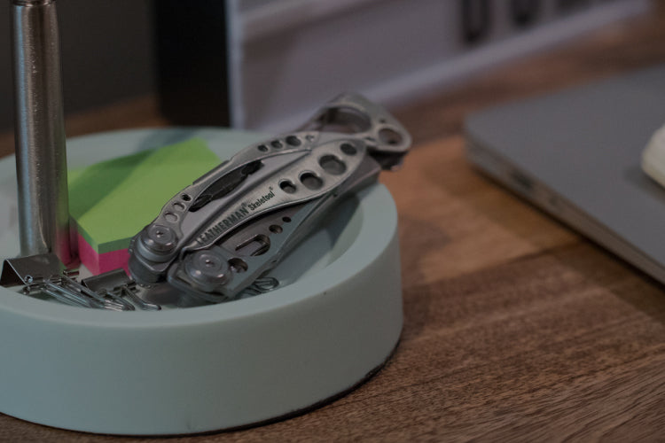 Translation missing: fr.Stainless Steel Leatherman Skeletool® resting on a desk organizer beside a notebook and sticky notes in a modern workspace.