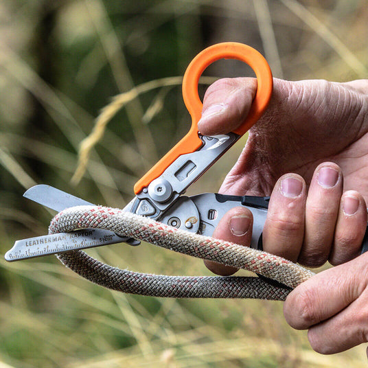 Translation missing: fr.A man using an orange and black Leatherman Raptor Rescue shears to cut a thick rope