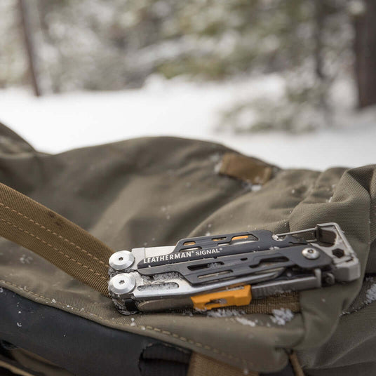 Translation missing: fr.A gray Leatherman Signal closed on a backpack surrounded by snow