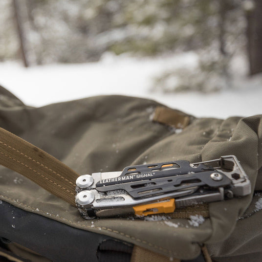Translation missing: en.A gray Leatherman Signal closed on a backpack surrounded by snow