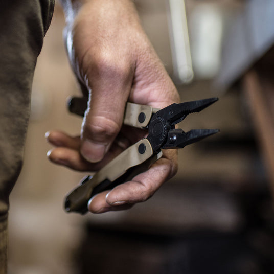A hand holding a Leatherman Coyote Tan Rebar® multi-tool with pliers, showcasing its versatile design for various tasks.