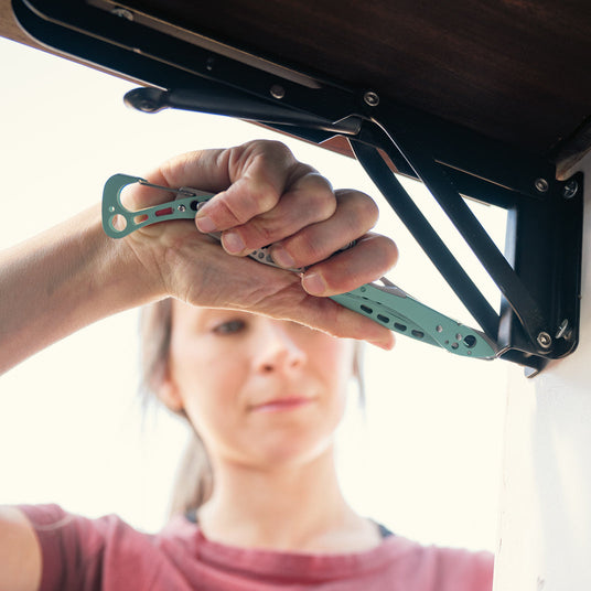 Translation missing: en.Person using a Leatherman Skeletool CX multi-tool to adjust hardware on a lift mechanism, shown in a close-up with focus on the tool in a compact, lightweight design