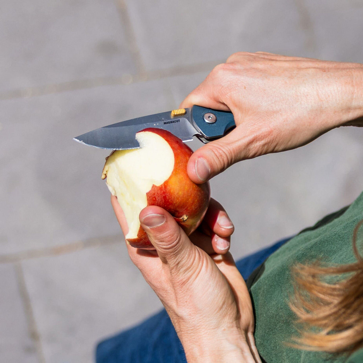Translation missing: en.Person using a Leatherman Blazer Denim folding knife to peel an apple outdoors, shown in a close-up view of the hands and knife in use