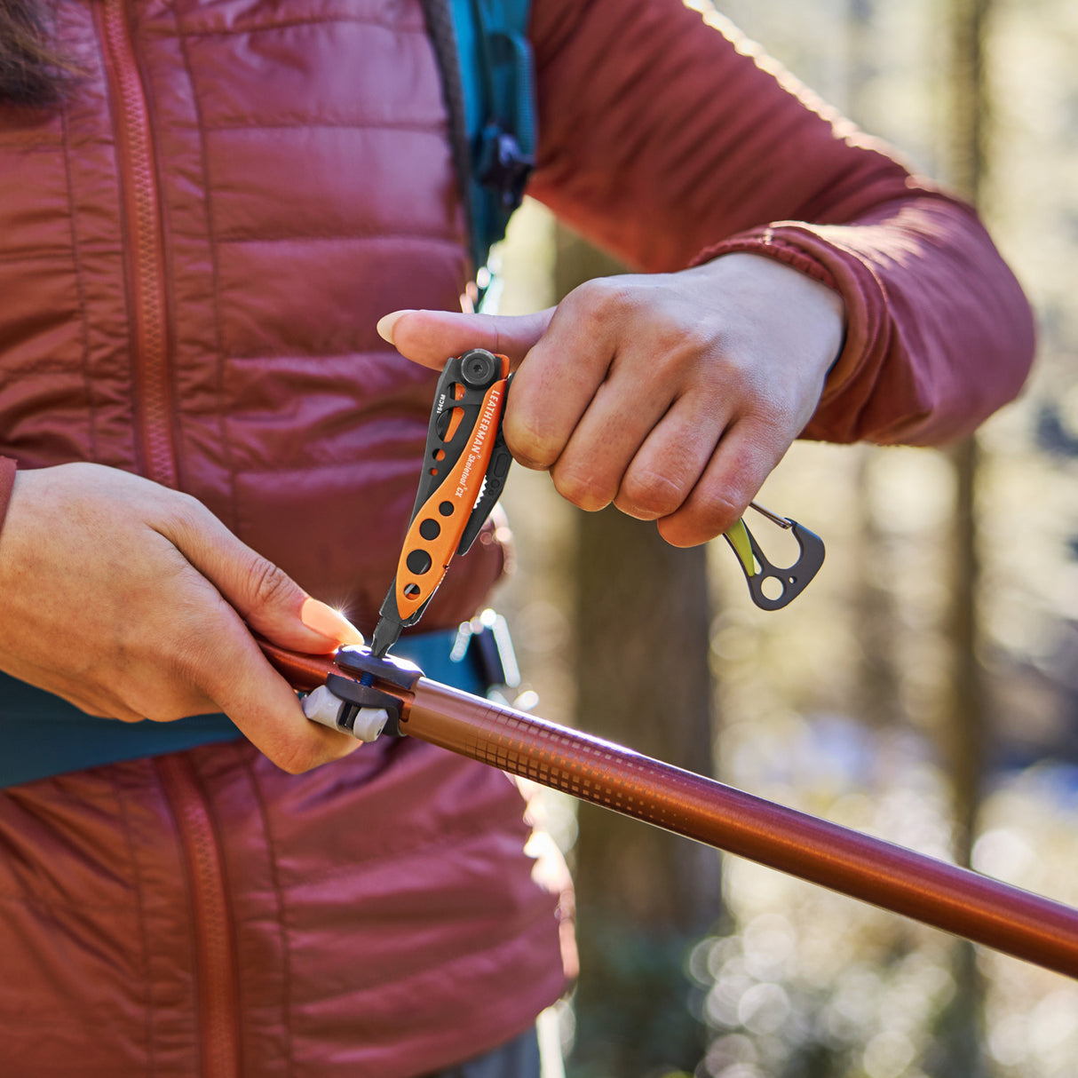 Translation missing: fr.Person using a Leatherman Skeletool® CX in Aurora color to adjust a hiking pole outdoors