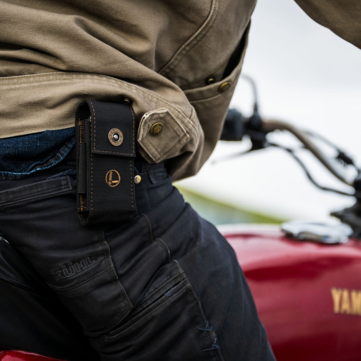 Translation missing: en.A man riding a motorcycle, wearing the Leatherman Black Bronze Nylon Sheath on his side, cruising down a scenic road