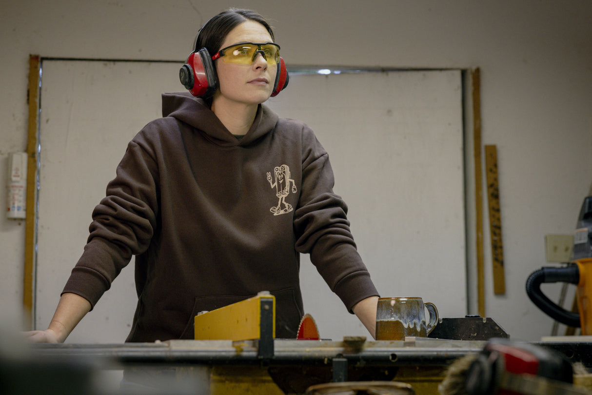 Translation missing: fr.A person wearing a brown Leatherman Mr. Wave hoodie standing at a workbench in a workshop, wearing safety glasses and earmuffs