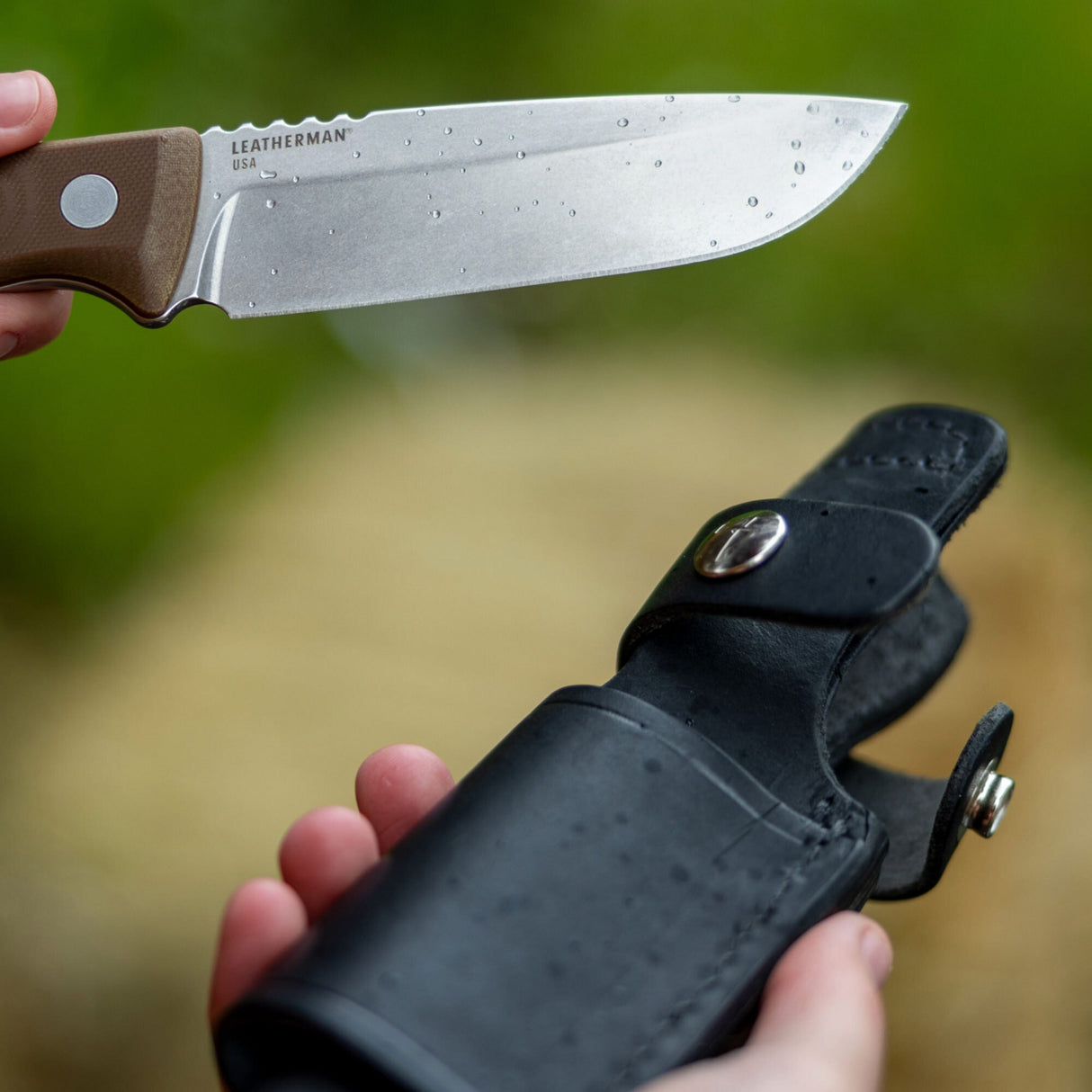 Translation missing: en.Earth Brown Leatherman Trac Knife with water drops on the blade held in one hand, while the Leatherman Trac Knife Sheath with silver snap closures open held in the other hand
