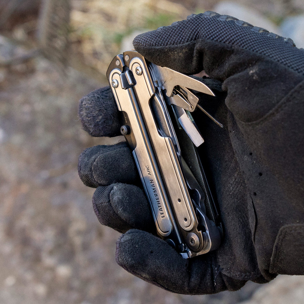 Translation missing: fr.Black DLC & Stainless Steel Leatherman ARC® held in a gloved hand, showcasing some tool included tools