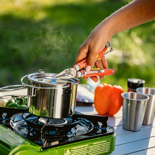 Translation missing: en.A person cooks on a stove, using Leatherman Signal to handle a pot filled with food
