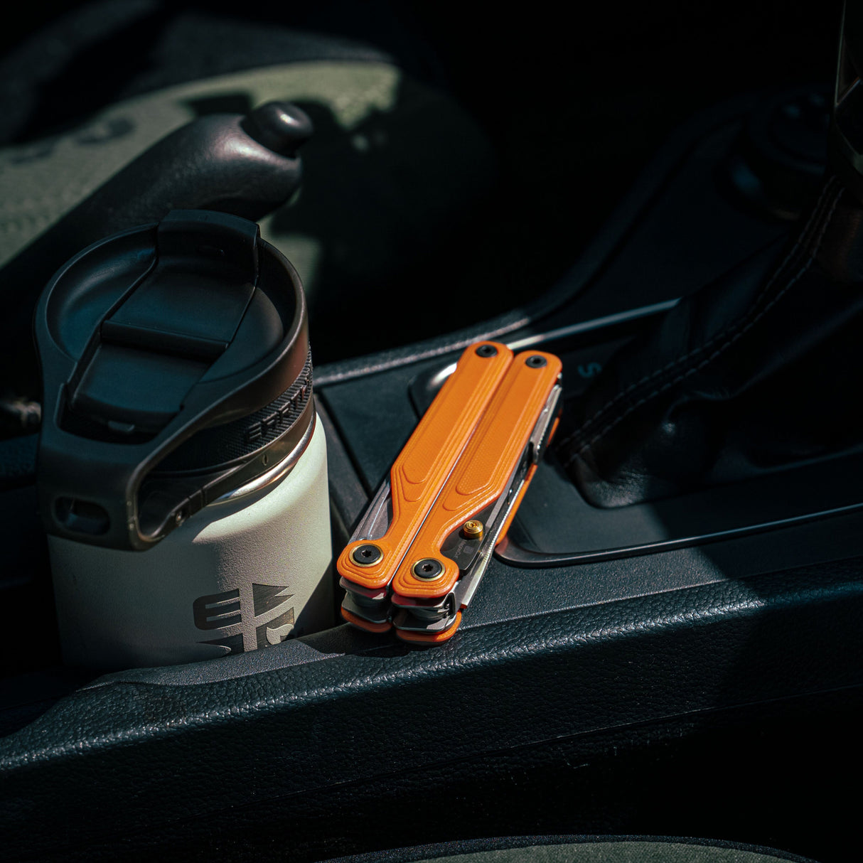 Translation missing: fr.Canyonland Leatherman Wave® Alpha multitool beside a stainless steel coffee mug in a car