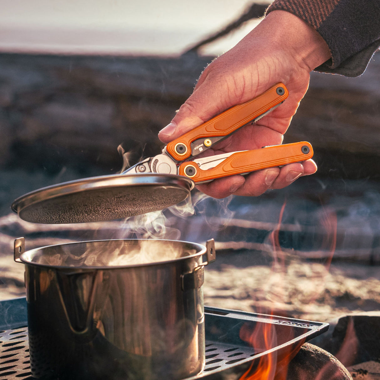 Translation missing: fr.Person using Canyonland Leatherman Wave® Alpha multitool to remove a lid from a pot while camping outdoors