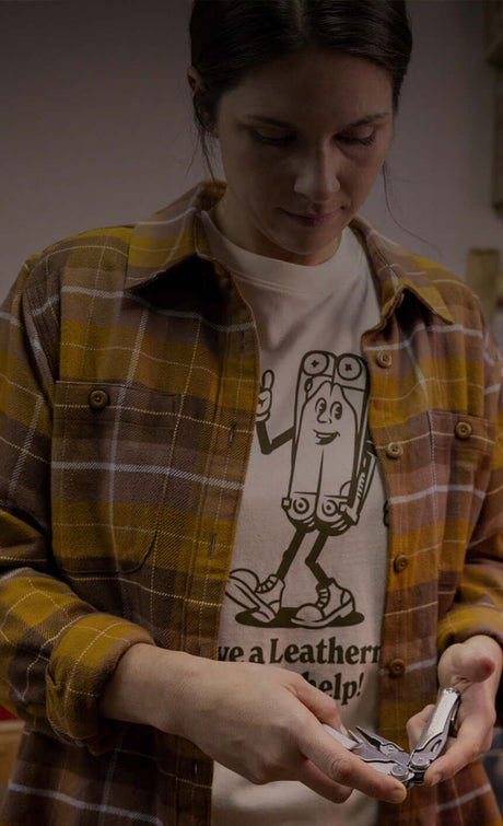 Translation missing: fr.Woman wearing a Leatherman Mr. Wave tee in Natural Raw color with a plaid button up shirt on top holding a stainless steel Leatherman multi-tool