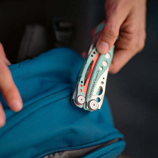 Translation missing: fr.Person holding closed Skeletool CX over a backpack