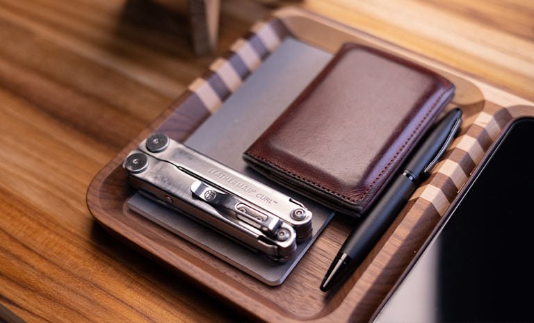 Translation missing: fr.Leatherman Curl, dark brown leather wallet and black pen on top gray notepad nicely arrange on wooden tray