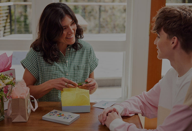 Translation missing: en.A mother opens Leatherman gift from son sitting at a table, capturing a moment of happiness and connection between them