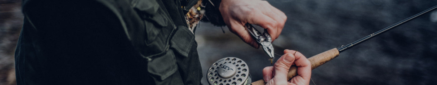 Translation missing: fr.A man using Leatherman Skeletool to tie a fly to his fishing rod, demonstrating his preparation for fly fishing