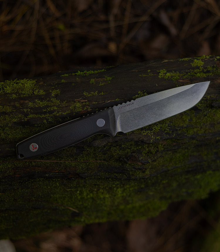 Translation missing: en.Leatherman Trac in soft focus, placed on a mossy log, showing off the state of the art Magnacut steel blade and g10 handle