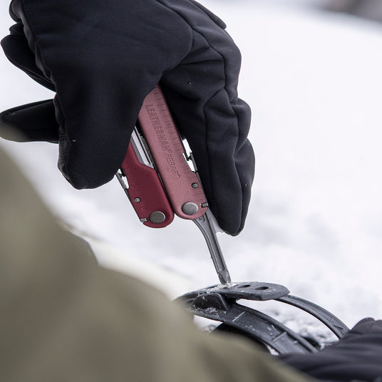 Translation missing: fr.Person wearing black gloves using a Leatherman Rebar in Heathered Cranberry color to tighten gear outdoors on a snowy surface