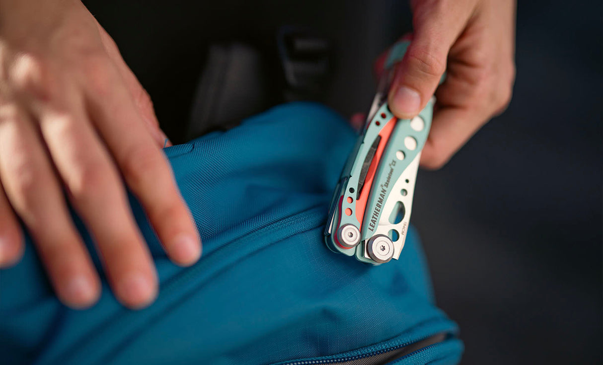 Translation missing: en.Hand holding a Paradise Skeletool® CX multitool while opening a blue backpack zipper
