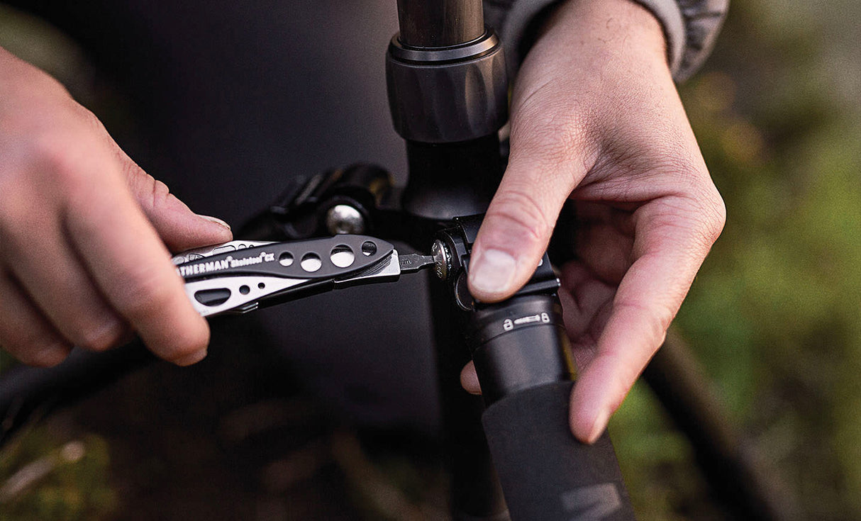 Translation missing: en.Hands using a Black & Stainless Skeletool® CX to tighten a bolt on a tripod outdoors