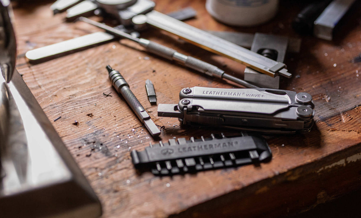 Translation missing: fr.Stainless Steel Leatherman Wave® Plus multi-tool on a workbench alongside a Leatherman bit kit, bit and bit driver extender