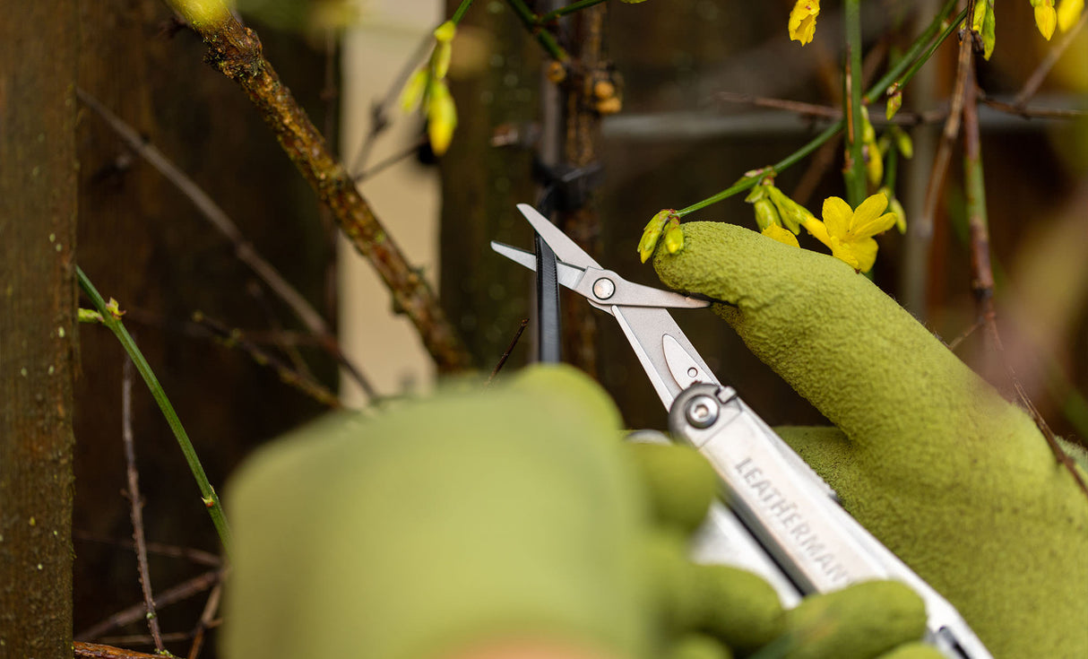 Translation missing: fr.Close-up of hands using a Stainless Steel Leatherman Wave® Plus scissors to cut a zip tie in a garden
