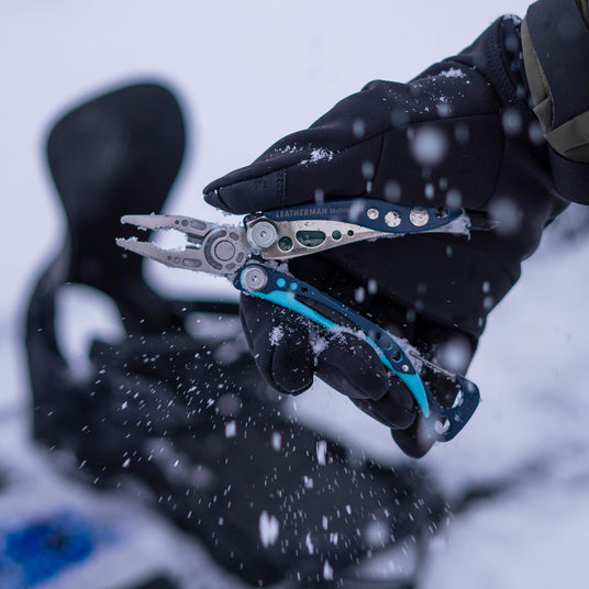 Translation missing: fr.Nightshade Leatherman Skeletool® CX pliers held in a gloved hand amidst falling snow in an outdoor setting