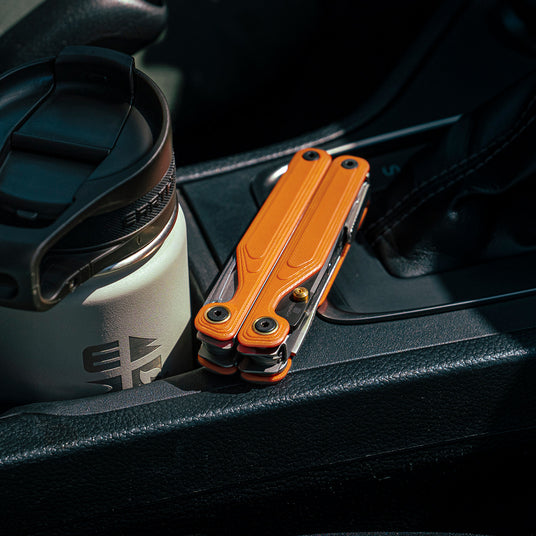 Translation missing: fr.Orange Leatherman Wave® Alpha multitool resting beside a coffee cup in a car's center console