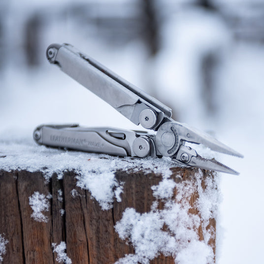 Translation missing: fr.Stainless Steel Leatherman Wave® Plus multi-tool resting on a snow-covered wooden stump in winter