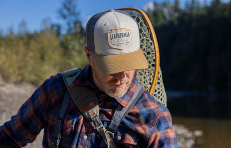 Translation missing: fr.Man wearing a Leatherman Pacific Northwest Trucker hat walking alongside a stream carrying a backpack and net