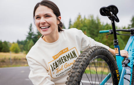 Translation missing: fr.Woman wearing a Leatherman Pacific Northwest crewneck, standing next to a bicycle outdoors