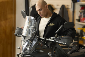 Translation missing: en.A person wearing a black Leatherman Vintage Zip-Up hoodie standing next to a motorcycle in a garage, with the hoodie’s gold Leatherman logo visible on the chest