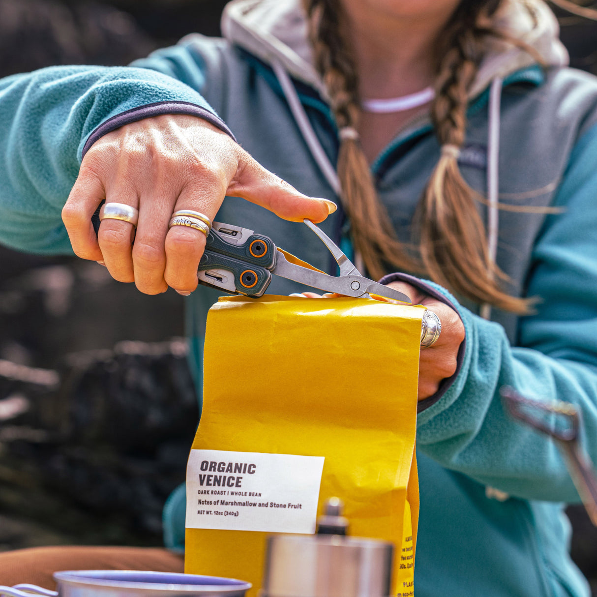 Translation missing: en.Person using the scissors on a Cascadia Leatherman Wave® Alpha to cut open a yellow bag of coffee beans outdoors