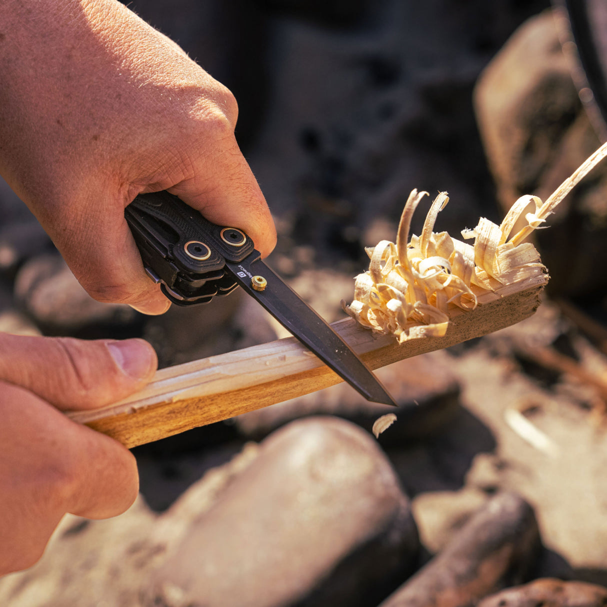 Translation missing: en.Person using the Obsidian Leatherman Wave® Alpha multitool to shave wood outdoors