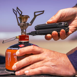 Translation missing: en.Close-up of a hand using an Obsidian Leatherman Wave® Alpha multitool to attach fuel to a camping stove