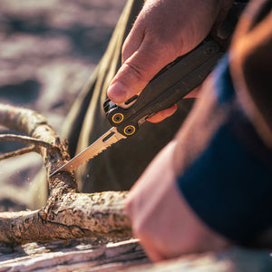 Translation missing: en.Person using the saw on an Obsidian Leatherman Wave® Alpha multitool to cut a branch outdoors