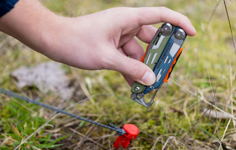 Translation missing: fr.A person uses Leatherman Signal to hammer tent stake in patch of grass