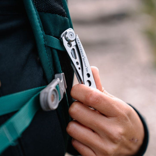 Person holding a closed Skeletool KBX that is attached to the strap of a backpack