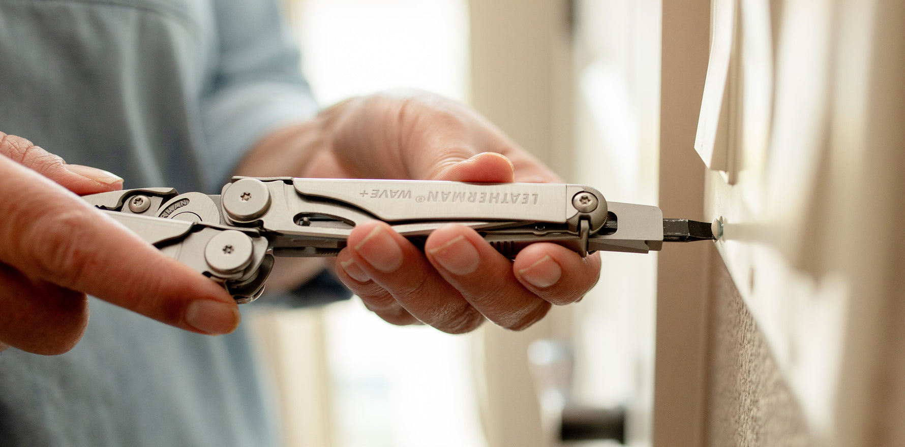 Person using a Leatherman Wave Plus multi-tool to screw on a light switch cover plate.