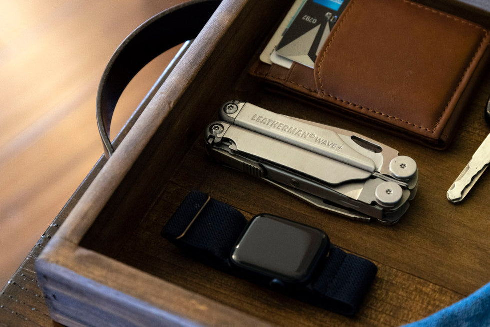 Leatherman Wave+ next to Apple watch, brown leather wallet and keys in wooden box.