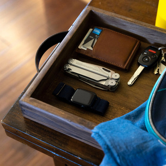 Leatherman Wave+ next to Apple watch, brown leather wallet and keys in wooden box.