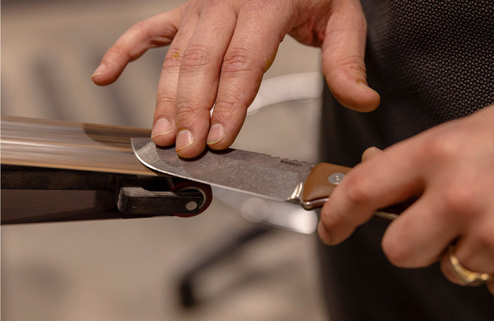 Translation missing: en.Close-up of a person sharpening a Leatherman Trac knife on a steel, showcasing knife maintenance techniques