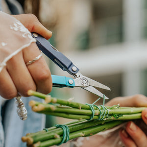 Translation missing: en.Person using the scissors on a Leatherman Micra® in Lavender Mist color to cut the rubber band holding flower stems