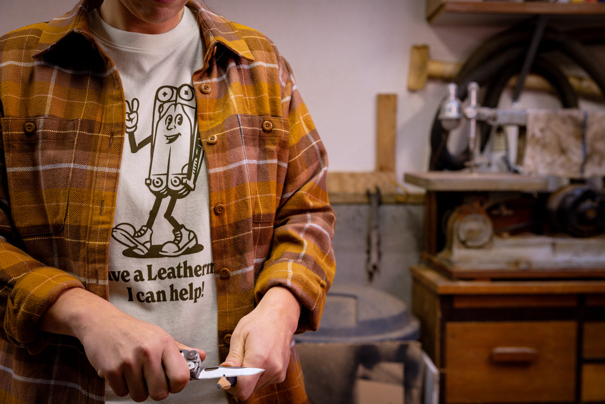 Translation missing: en.A person wearing a natural-colored Leatherman Mr. Wave Tee with a cartoon multitool design using a Leatherman multitool to sharpen a pencil