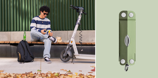 Translation missing: en.A man using the scissors on a Micra® multitool in Cardamom color to open a food packet while sitting on a bench next to a backpack and electric scooter