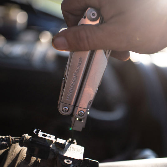 Close-up of a hand using a Leatherman Surge to work on a small mechanical device.