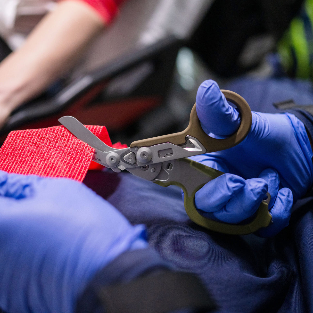 Translation missing: en.Person using the shears on a Woodland Leatherman Raptor® Rescue to cut a piece of red gauze
