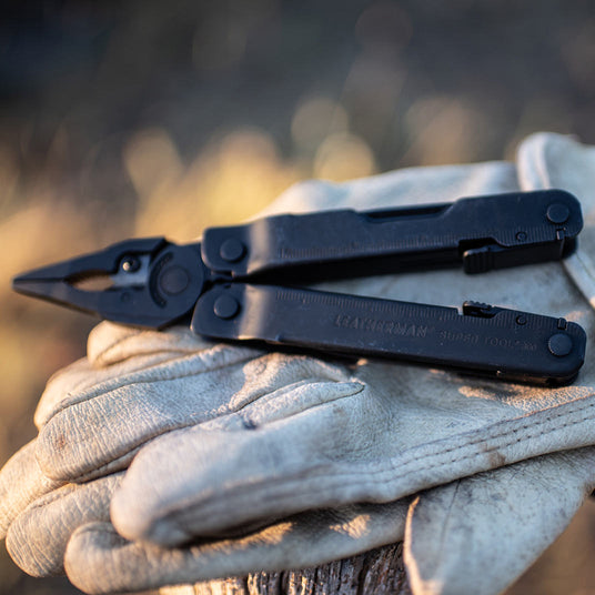 Translation missing: fr.Leatherman Super Tool 300 multi-tool in black resting on beige gloves, showcasing its rugged design and functionality