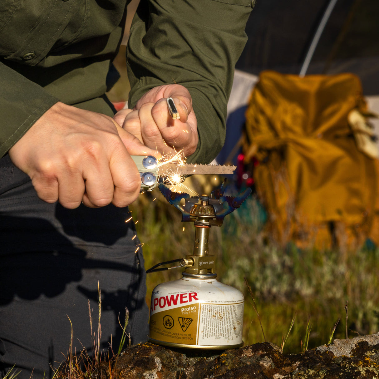 Translation missing: en.Hands using a Sandstorm multitool to strike sparks onto a small camping stove outdoors
